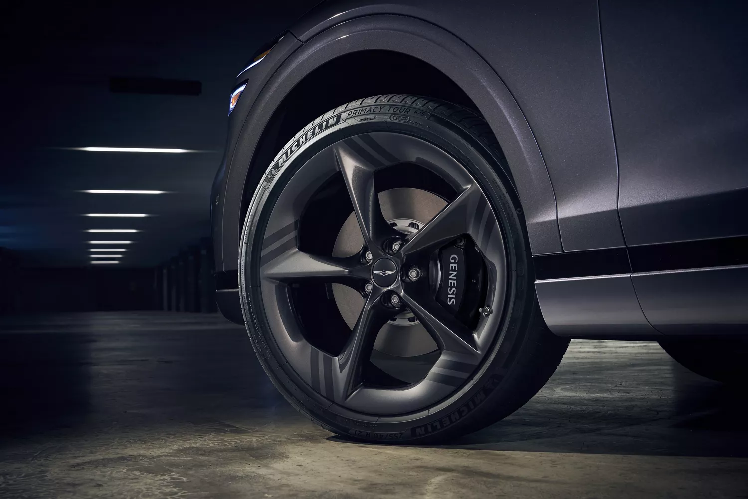 A low-angle shot of a dark-colored Genesis car wheel and tire in a dimly lit parking garage.