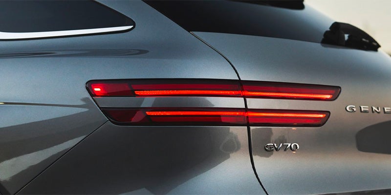 Close-up of a gray Genesis GV70 SUV's rear, showing its distinctive horizontal red LED taillights.