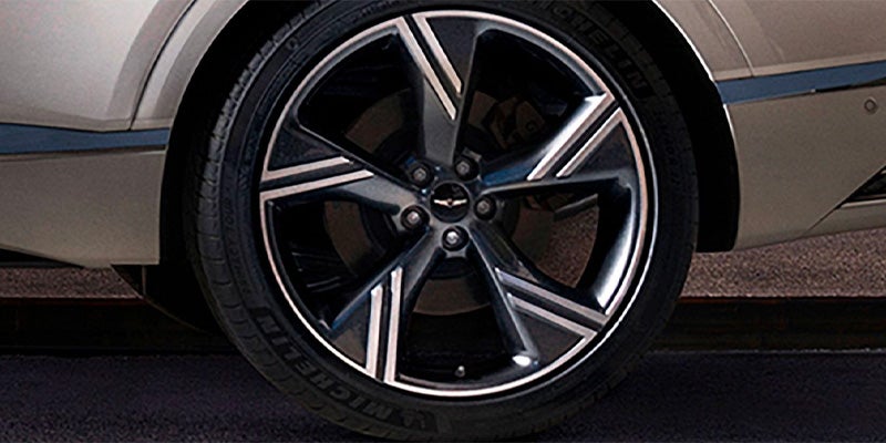 Close-up of a dark gray car wheel with black and silver multi-spoke rims on a dark road.