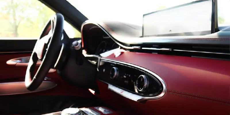 Interior view of a car with a black steering wheel, red dashboard, and a large horizontal screen.