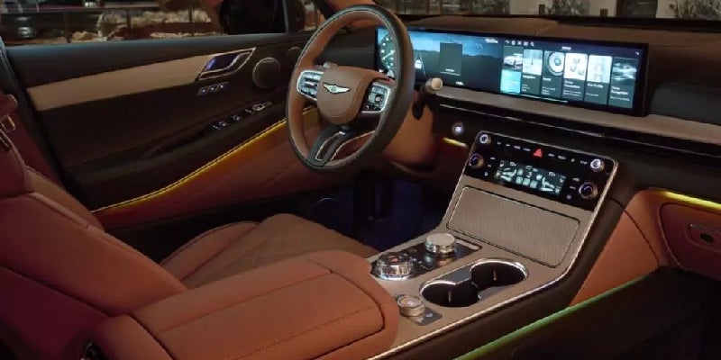 Modern luxury car interior with tan leather, a wide digital display, and ambient strip lighting.