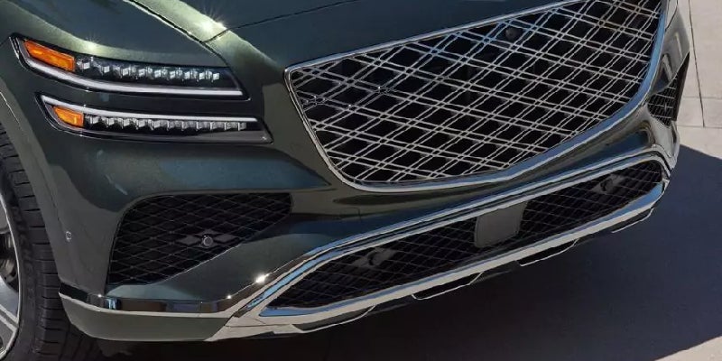 Front view of a dark green car with thin bright LED headlights, a large diamond-patterned chrome grille.